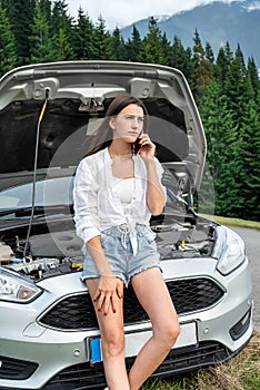 woman talking over a phone stand near broken car at road
