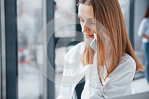 Woman talking by phone in front of group of young successful team that working and communicating together indoors in