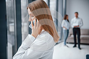 Woman talking by phone in front of group of young successful team that working and communicating together indoors in