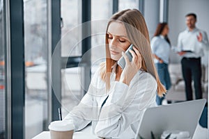 Woman talking by phone in front of group of young successful team that working and communicating together indoors in