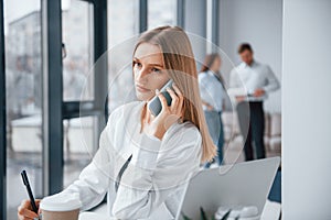 Woman talking by phone in front of group of young successful team that working and communicating together indoors in