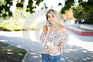 Woman talking by phone outdoors in city street. Portrait of young smiling girl standing with smartphone