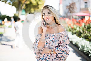 Woman talking by phone outdoors in city street. Portrait of young smiling girl standing with smartphone