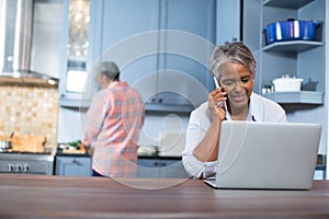 Woman talking on phone while using laptop