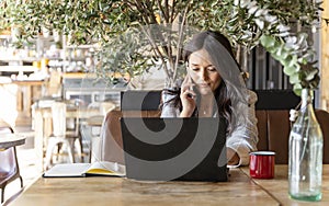 Woman talking on the phone while working online with a laptop computer in a coffee shop