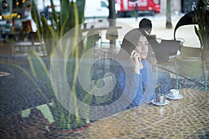 Woman talking on smart phone while sitting in cafe seen through window