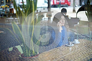 Woman talking on smart phone while sitting in cafe seen through window