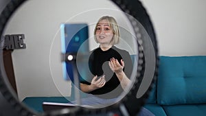 Woman talking to camera and recording video with smartphone and ring light lamp at home, vlogger