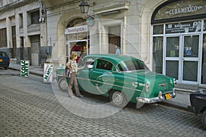 Woman talking to driver of old green car in Old Havana, Cuba