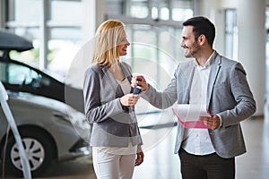 Woman is talking to handsome car dealership worker while choosing a car