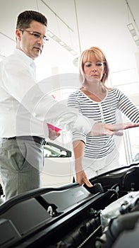 Woman is talking to handsome car dealership worker while choosing a car
