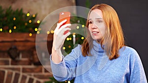 Woman is talking on a video link near the Christmas tree. congratulates friends