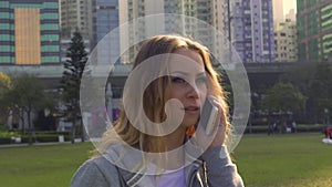 Woman talks on cellphone on fresh green meadow in city park
