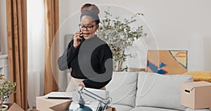 A woman talks on phone while staring into screen of laptop that sits on cardboard moving boxes girl has conversation