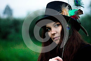 A woman in a tall hat with a peacock feather in her hands