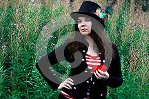 A woman in a tall hat with a red knitted heart in her hands