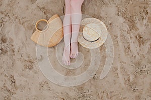 Woman tanned legs, straw hat and bag on sand beach. Travel concept. Relaxing at a beach, with your feet on the sand