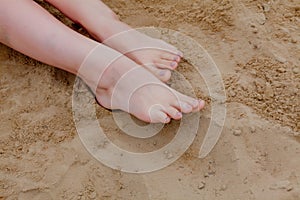 Woman tanned legs, straw hat and bag on sand beach. Travel concept. Relaxing at a beach, with your feet on the sand