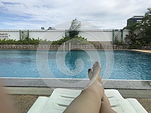 Woman tanning legs relaxing in beach chairs. Girl`s legs resting in a pool. The hotel public swimming pool.