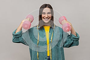 Woman with tape measure on shoulders holds dumbbell going sport to reduce extra centimeters on body.