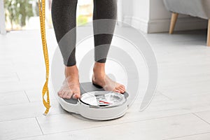 Woman with tape standing on scales indoors, space for text. Overweight