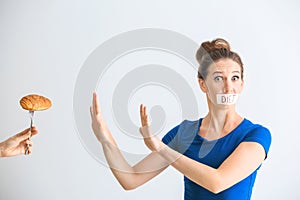 Woman with taped mouth refusing to eat unhealthy food on white background. Diet concept