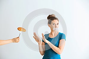 Woman with taped mouth refusing to eat unhealthy food on white background. Diet concept