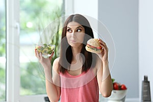 Woman with tasty burger and fresh salad indoors. Choice between healthy and unhealthy food