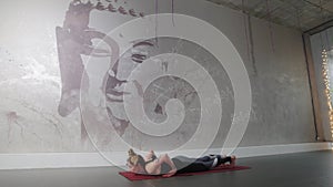 A woman with tattoos is engaged in aerobics against the background of a wall with the image of a Buddha