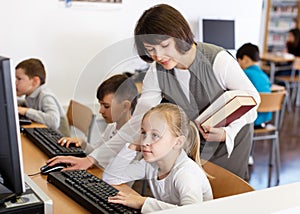 Woman teacher helping tween girl in computer class