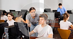 Woman teacher helps guy with learning on computer in school