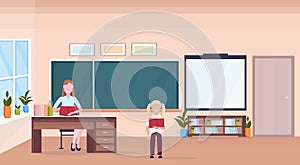 Woman teacher sitting at desk schoolgirl reading book education concept modern school classroom interior chalk board