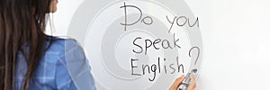 Woman teacher writes with marker do you speak english on white board