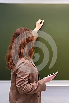 Woman teacher writes a text in chalk on a school blackboard