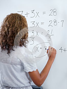 Woman, teacher and writing on whiteboard for mathematics, numbers or equations in classroom. Rear view of female person