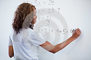 Woman, teacher and writing on whiteboard for maths, numbers or equations in classroom. Rear view of female person