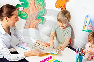 Woman teaches little kids to read letters in the book