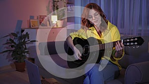 woman teaches online guitar playing using remote lessons online sitting on couch at home