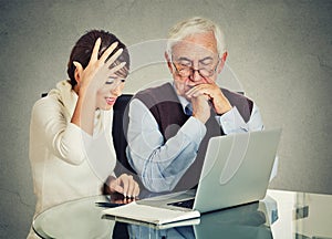 Woman teaching confused elderly man how to use laptop