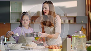 Woman teaching daughter to sieve flour on dough at kitchen