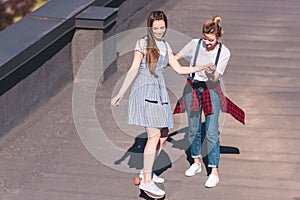 woman teaching her female friend riding on skateboard