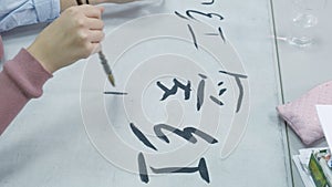 Woman teaching teen how to write Chinese characters at calligraphy class. Student learning writing with brush, ink, and