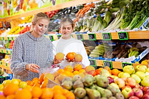 Woman with teen daughter who came to the supermarket for shopping, choose oranges at counter