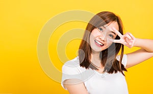 Woman teen smile standing wear t-shirt showing finger making v-sign symbol near eye