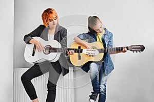 Woman and teenager playing guitars near wall