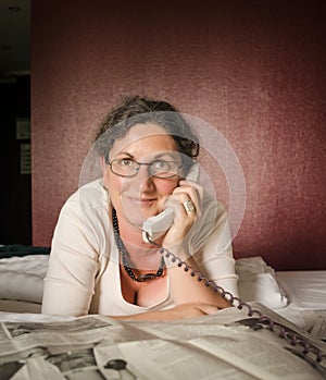 Woman on telephone in front of newspaper on bed