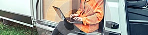 Woman teleworking sitting in the door of a camper van