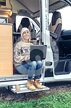 Woman teleworking sitting in the door of a camper van