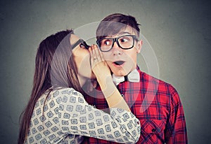 Woman telling whispering secret gossip in the ear to an amazed shocked man