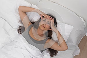 woman, temple pain evident, gently massages her head, battling a headache in a well-lit bed photo